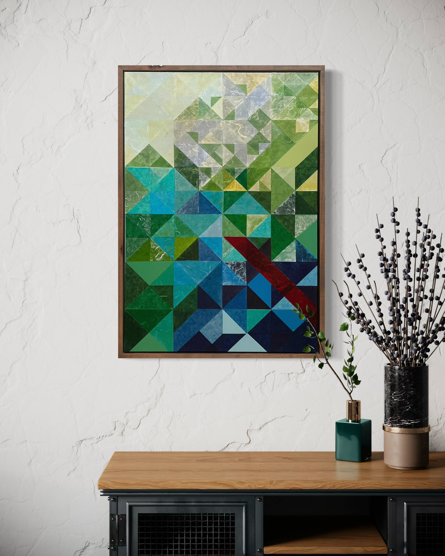 Geometric abstract art piece on a white wall above a wooden table with decorative plants.
