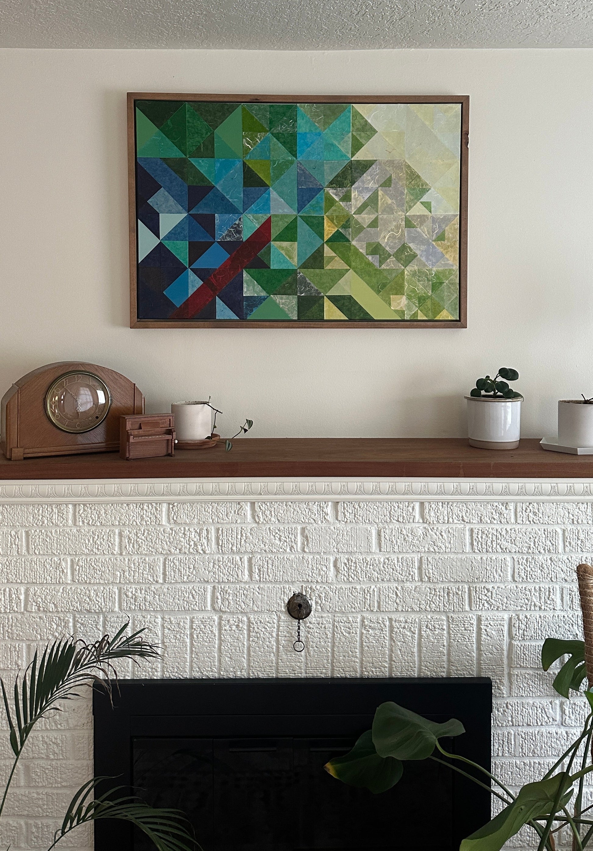Geometric abstract art on a wall above a fireplace with decorative items.