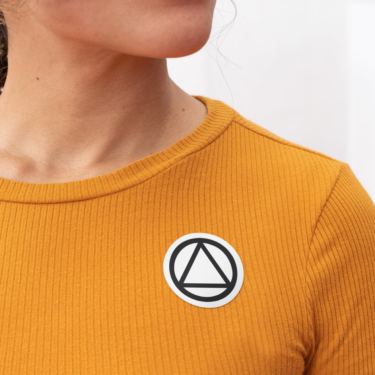 Recovery symbol sticker worn on a mustard ribbed shirt